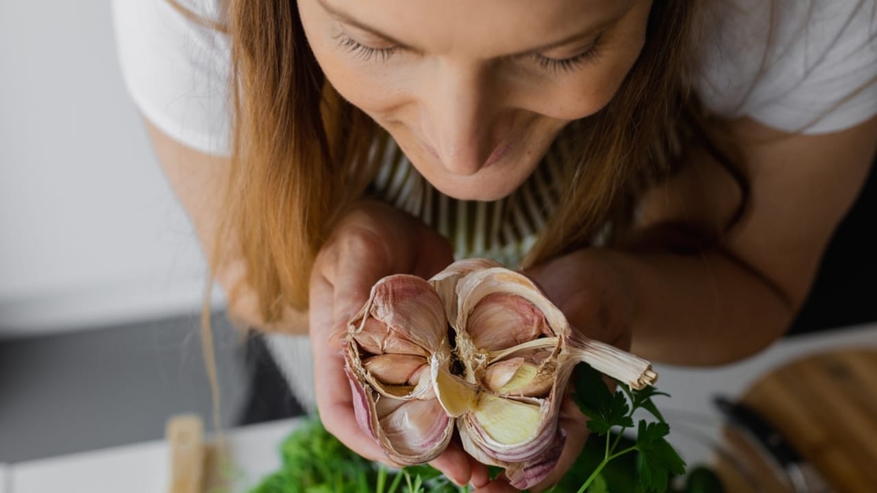 Improve Your Skin Naturally by Adding Garlic to Your Skincare Routine - woman smiling holding garlic ss2170612481